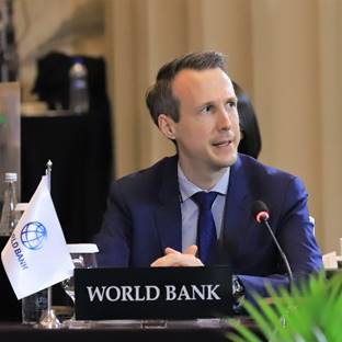 A person in a suit sitting at a podium

Description automatically generated